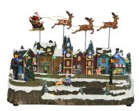 Lumineo mozgó, zenélő karácsonyi falu dekoráció felette repülő Mikulással, adapterrel és LED világítással 38x15x25,5 cm